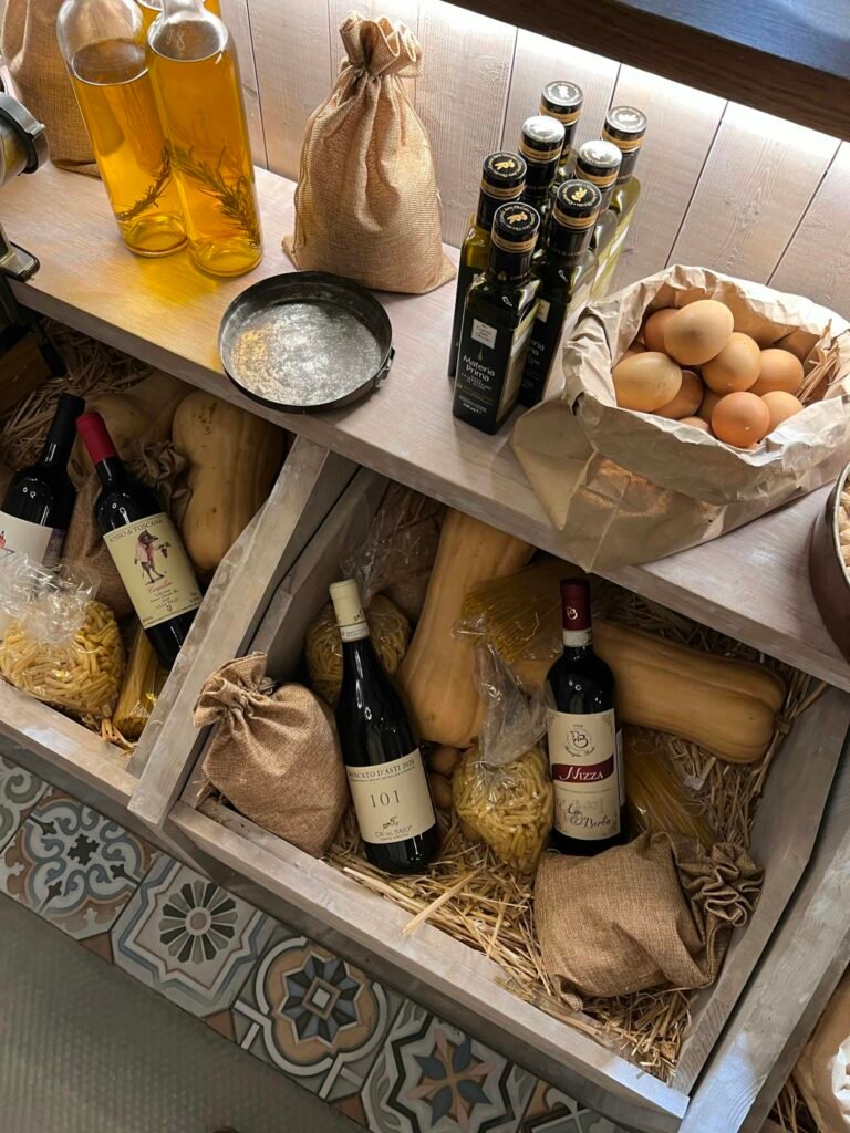 A rustic wooden store display featuring wine, olive oil, pasta, and fresh eggs.
